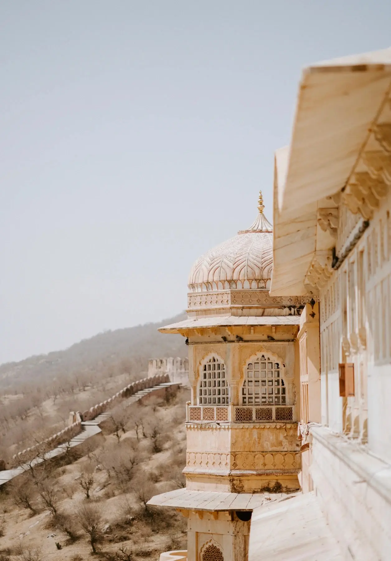 A carved sandstone palace balcony overlooking hills in soft morning haze