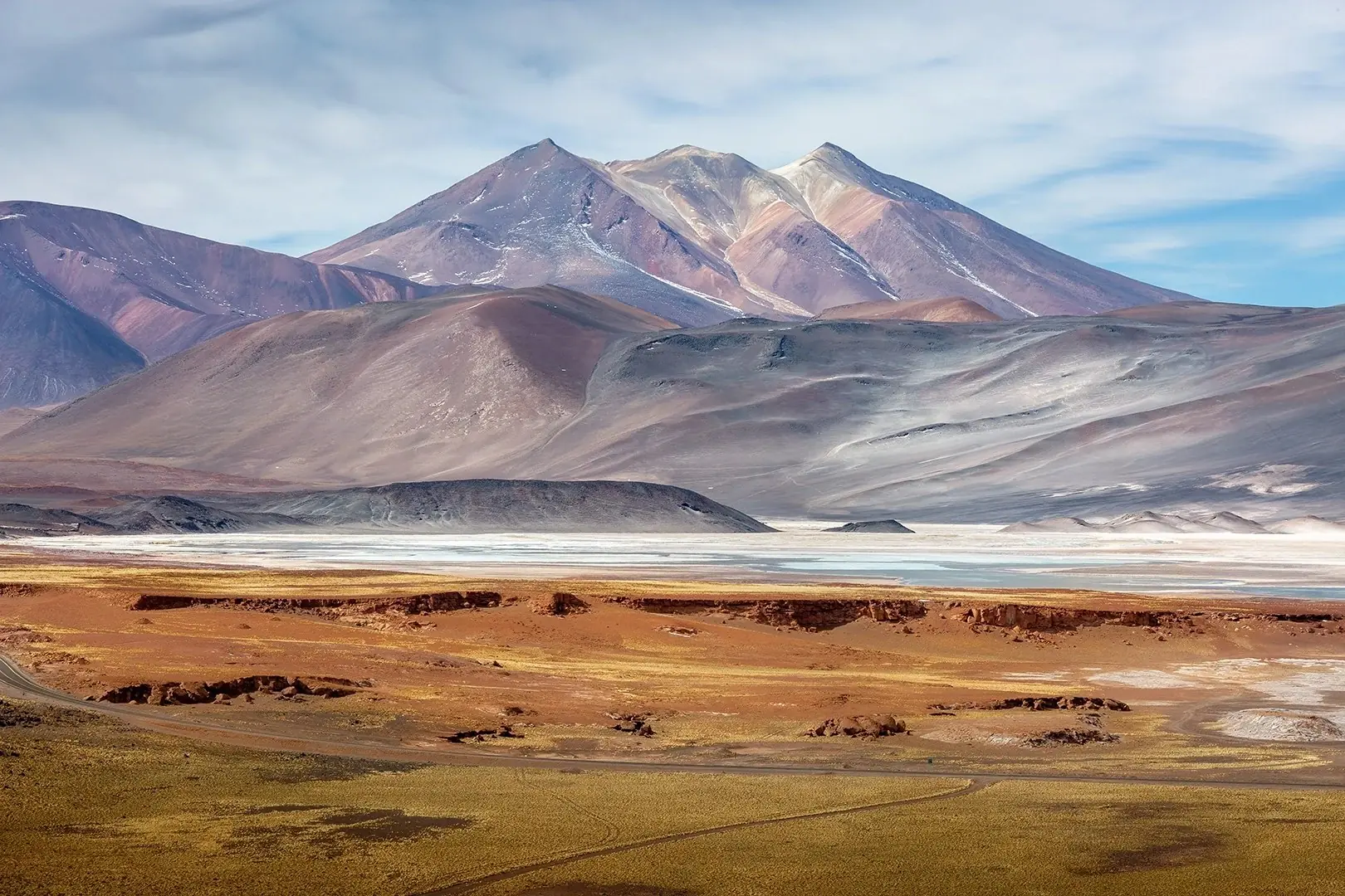 A snow-dusted volcano above the pink and ochre plains of the Atacama desert