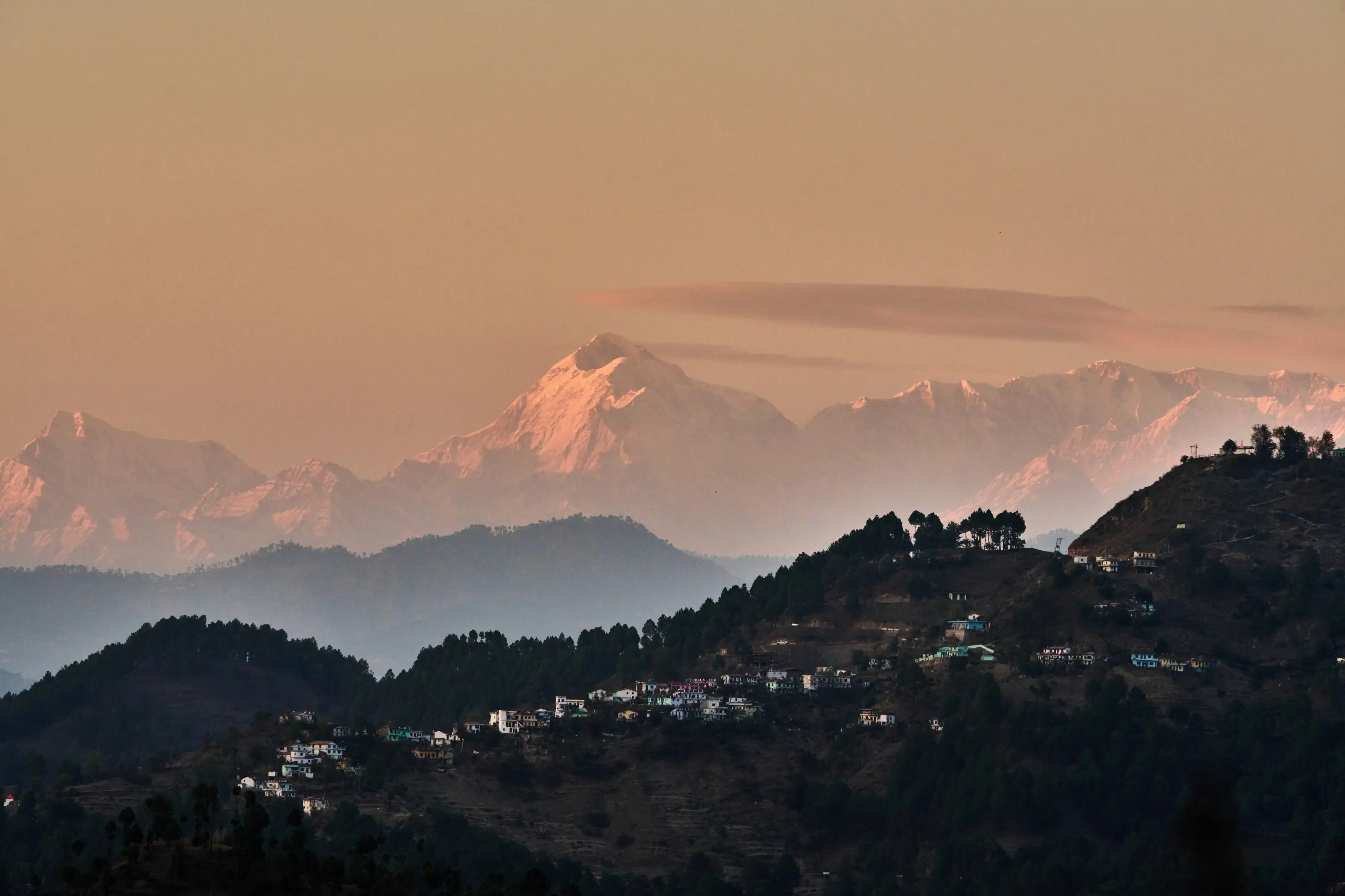 Snow peaks of the Himalaya glowing pink at sunset above wooded hills