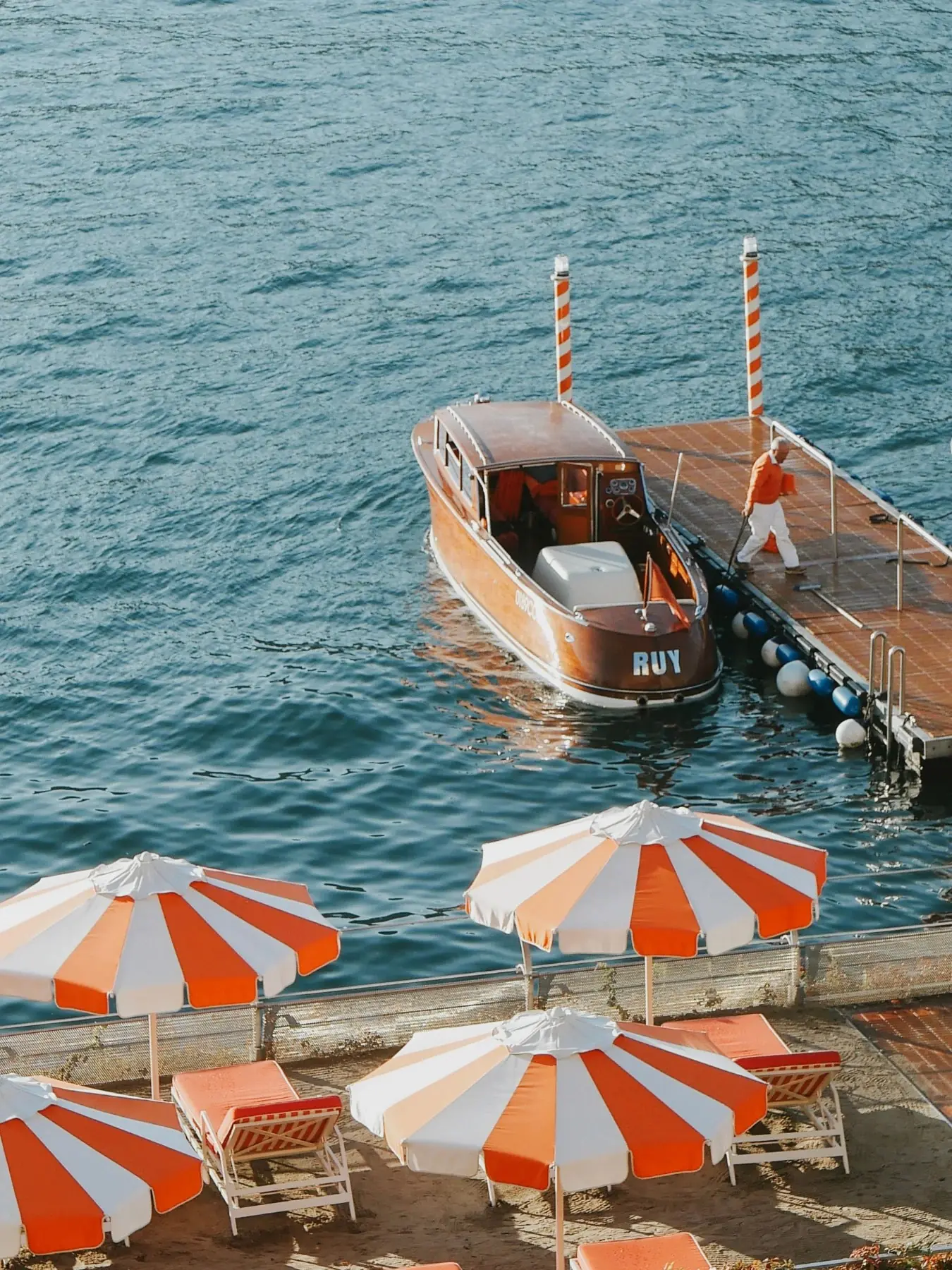 A wooden motorboat at a jetty beside orange and white striped parasols on the lake