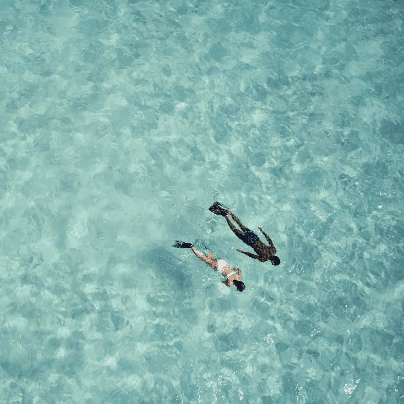 Two people swimming in clear turquoise water, seen from above