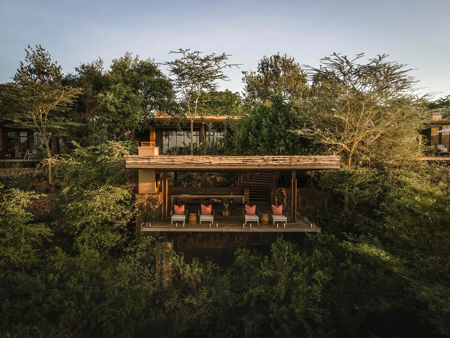 A wooden safari lodge raised among acacia trees at dusk
