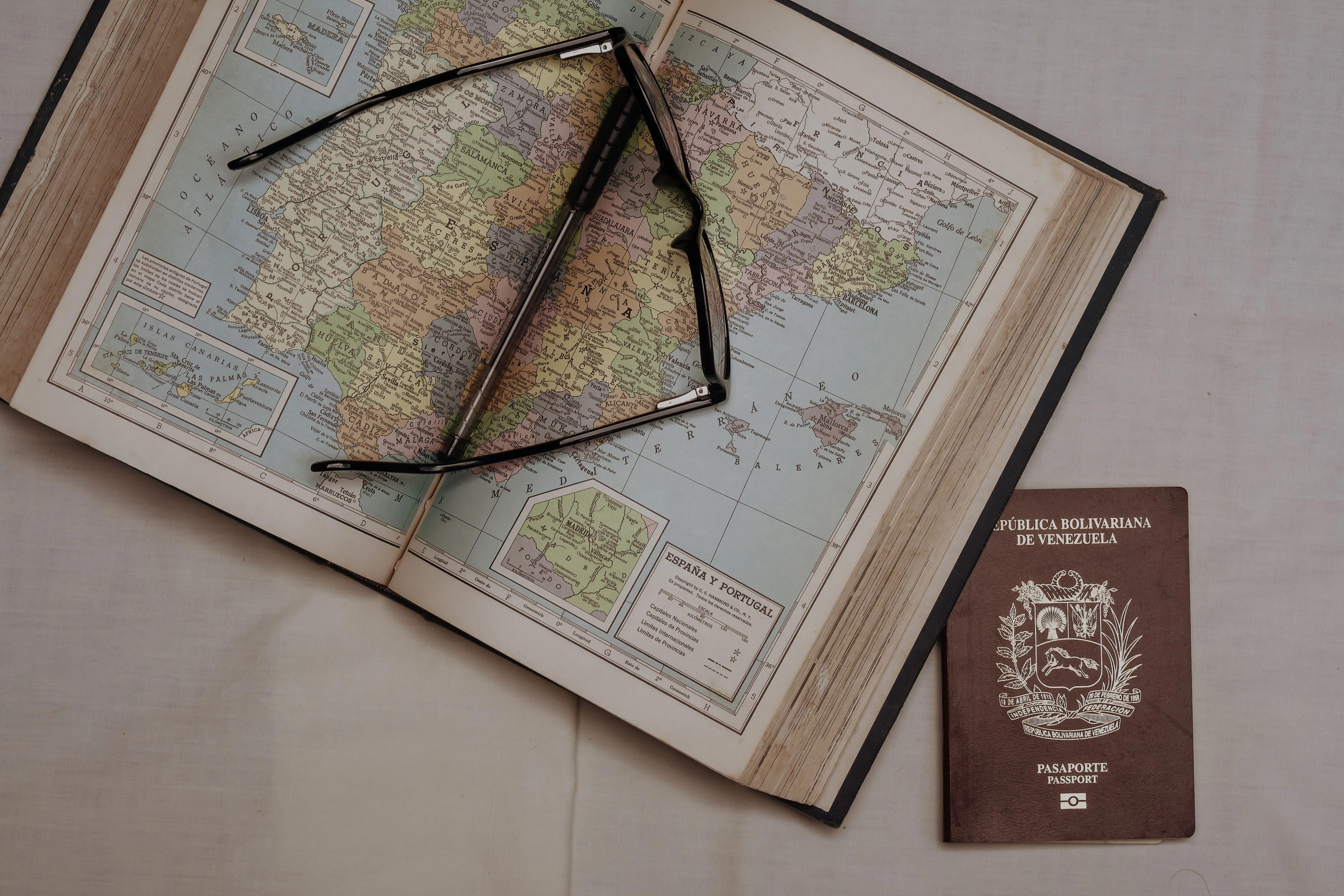 An open atlas beside reading glasses and a passport