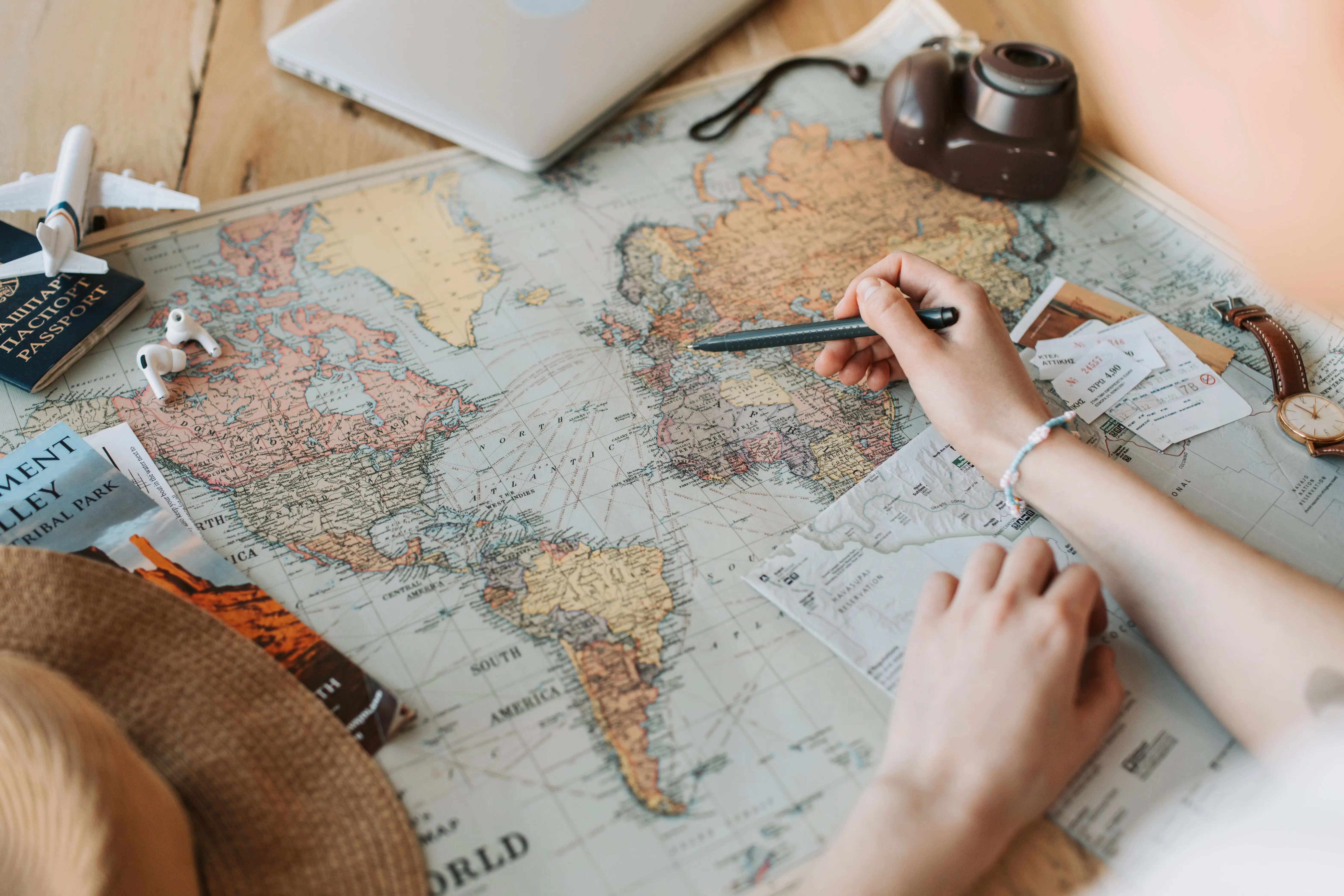 Hands tracing a route across a world map beside a notebook and a cup of coffee