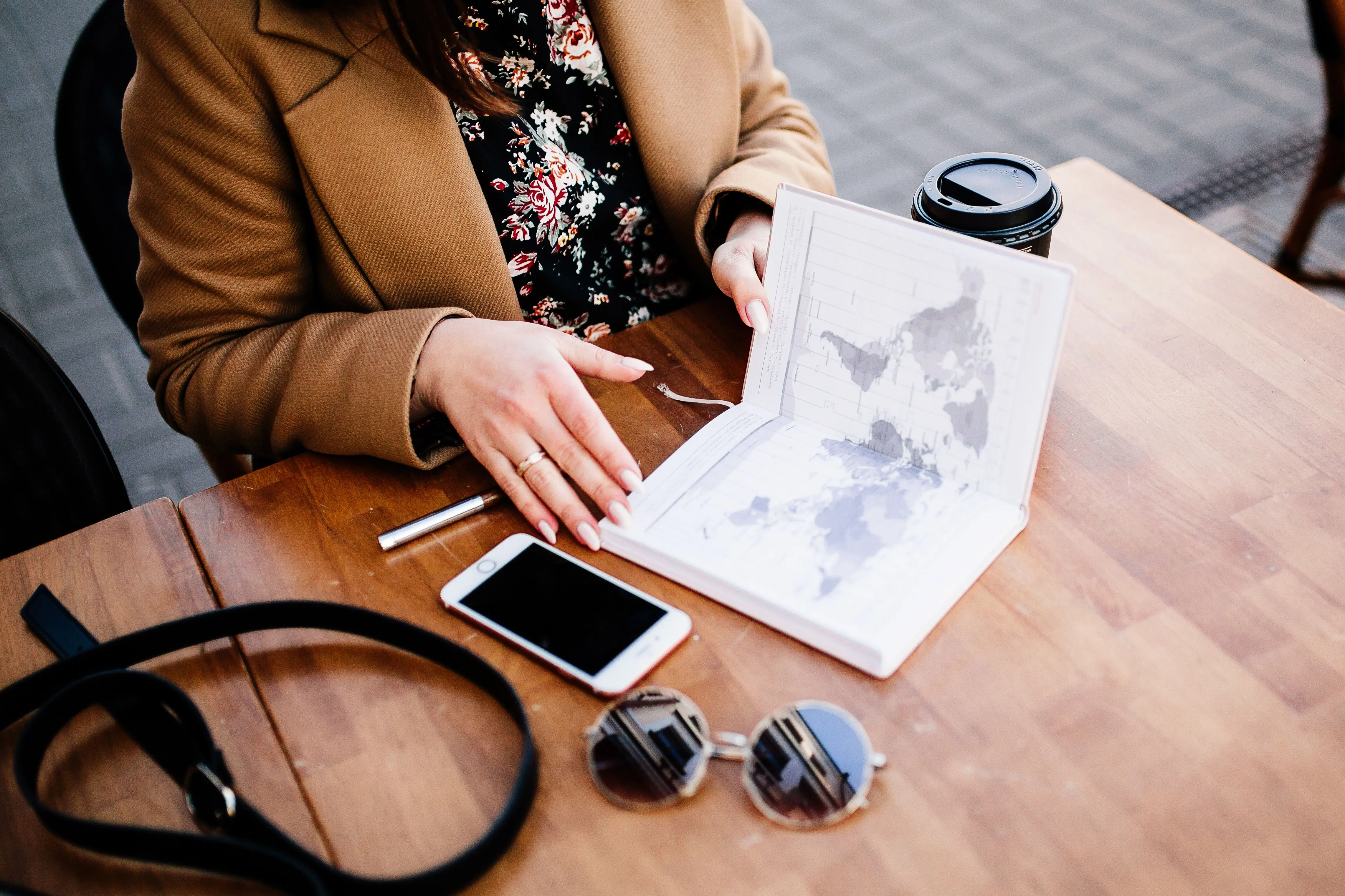 A woman at a cafe table with a world map notebook, a phone and sunglasses
